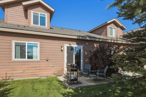 Una casa de dos pisos con un patio techado, una parrilla y mobiliario exterior.