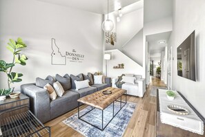 A modern living room with a grey sectional sofa, a wooden coffee table, and a staircase leading to another level. - The Donnelly Den | Tamarack Getaway, Game Room (Donnelly)