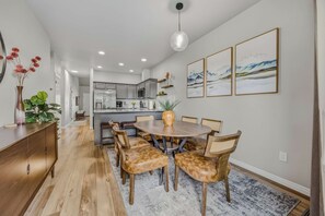 A modern kitchen with grey cabinets, a central island, and a dining area with a round table and leather chairs. - The Donnelly Den | Tamarack Getaway, Game Room (Donnelly)