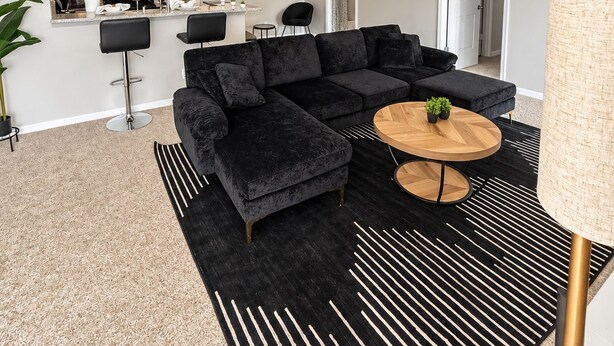 Un salon moderne avec un canapé d’angle, une table basse ronde et un coin cuisine à l’arrière-plan.