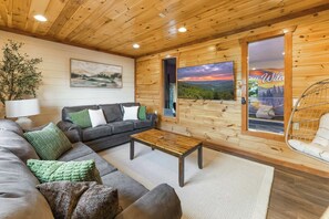 Ein gemütliches Wohnzimmer mit einer Couch, einem Couchtisch und Blick ins Freie durch eine Glasdoor.