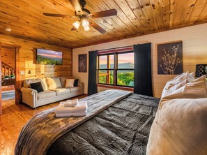 Ein gemütliches Zimmer mit einem Bett, einer Couch, einem Deckenventilator, einem Fenster mit Blick und Kunstwerken an den Wänden.