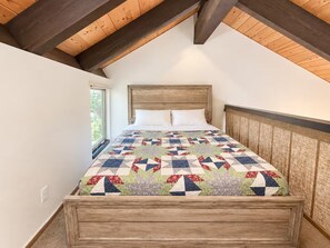 Ein Schlafzimmer mit einem hölzernen Kopfteil, einer Stegdecke mit geometrischem Muster und einem Fenster, das natürliches Licht hereinlässt.