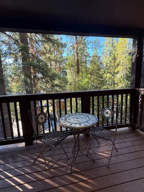 Eine Holzterrasse mit einem runden Tisch und zwei Stühlen, umgeben von einem Geländer mit Blick auf einen Wald.