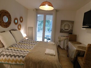 A hotel room with a bed, a television, a table with a chair, and a view of the outdoors through a door.