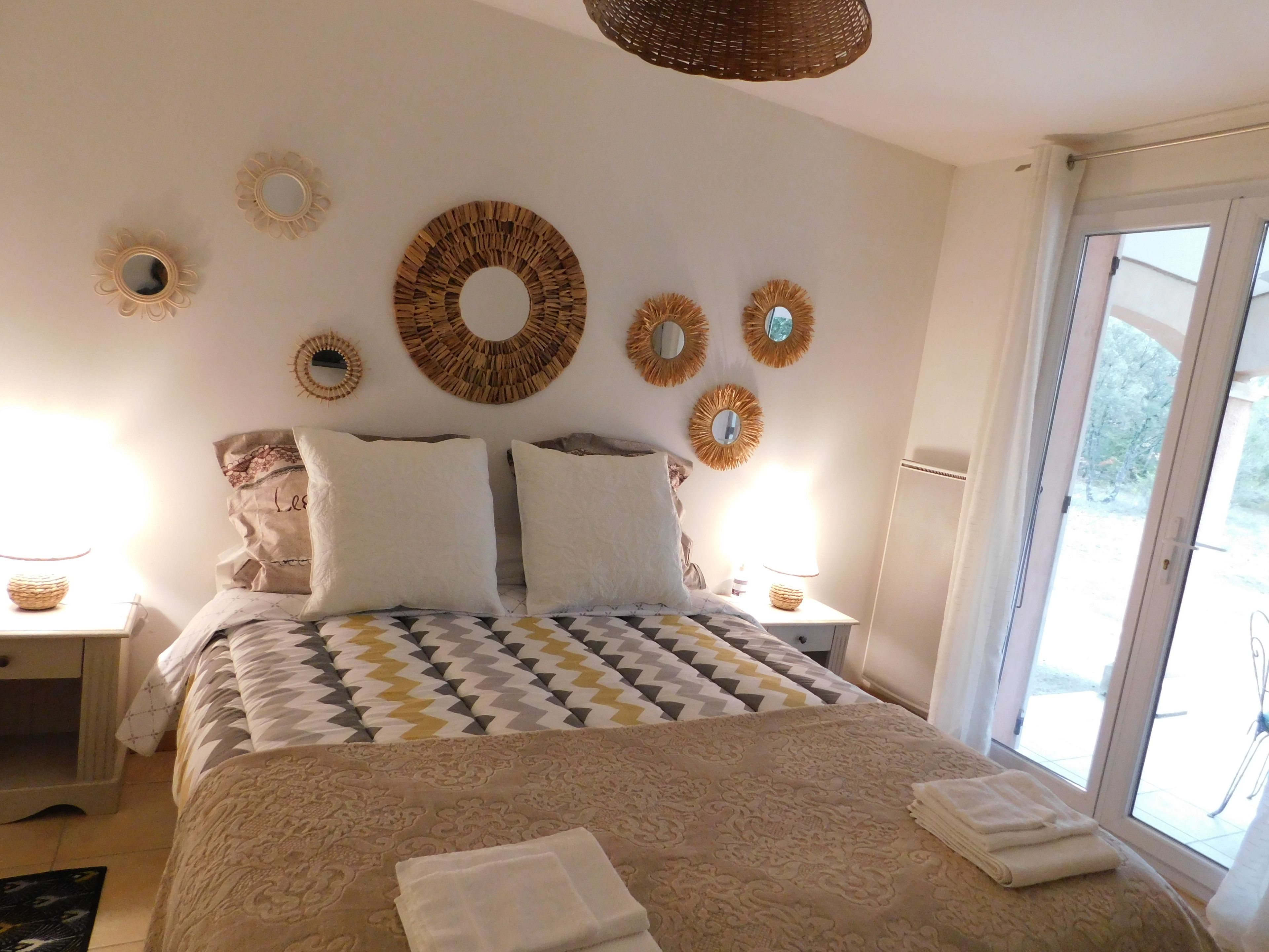 Ein Schlafzimmer mit einem Bett, Kissen, einem Nachttisch mit Lampe und dekorativen Wandspiegeln.