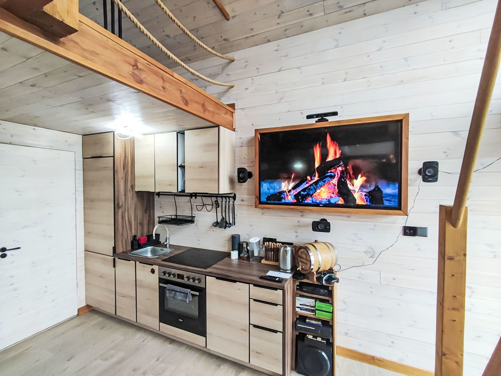 Une cuisine moderne avec des meubles en bois, un four encastré et un téléviseur à écran plat fixé au mur.