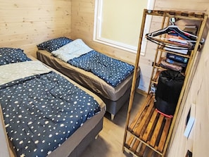 A room with two beds, a window, and a wooden rack with hanging items.