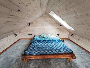 A small, sloped-roofed attic bedroom with a wooden bed and a skylight.