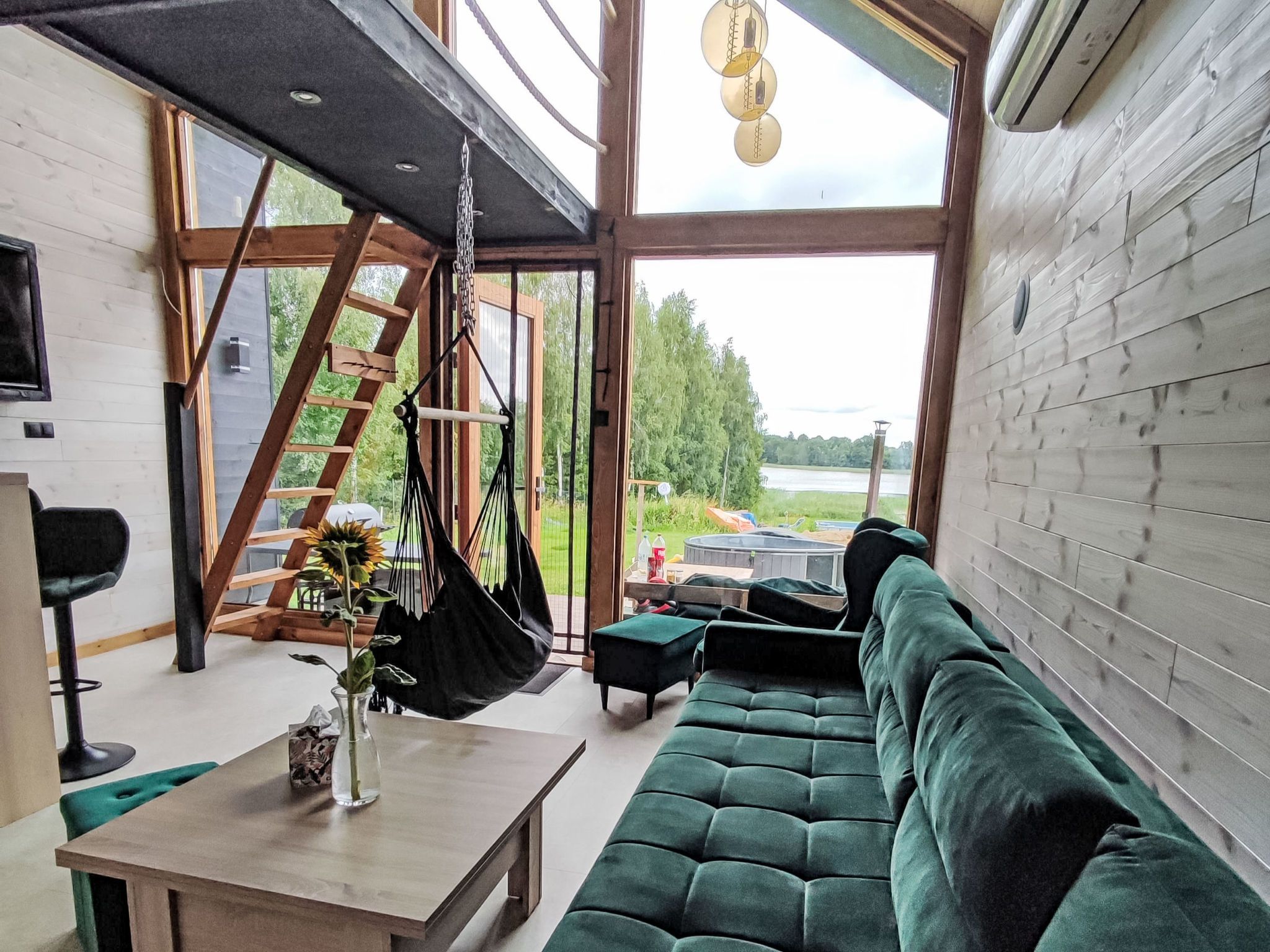 A modern interior with a green sofa, a hanging chair, and a wooden staircase.