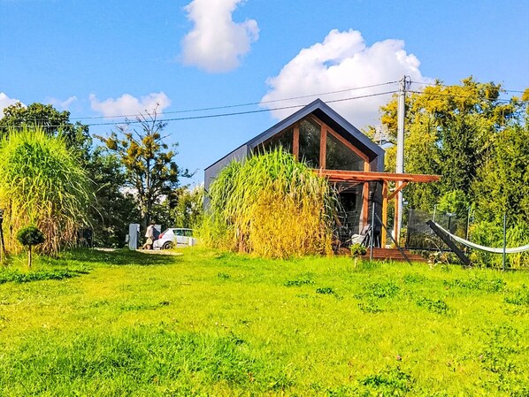 A modern house with a large glass window, surrounded by lush greenery and a clear sky.