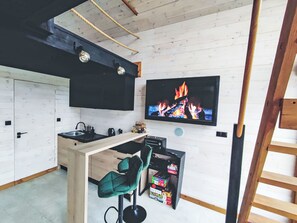 A modern kitchen with a wooden ceiling, a TV mounted on the wall, and a bar area with stools.