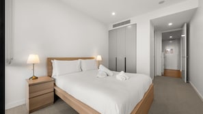 Une chambre d’hôtel avec un lit, des tables de chevet, une armoire et une salle de bain visible à travers une porte ouverte.