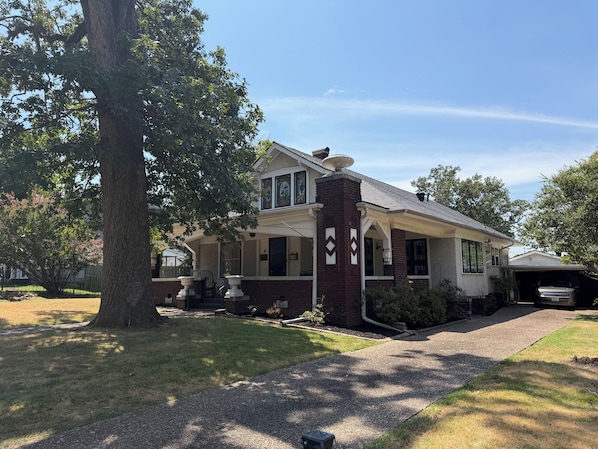 A two-story house with a brick chimney, a covered porch, and a driveway leading to a garage. - 4bed 2ba bungalow for a relaxing stay just a short drive from museums, food &FSM (Fort Smith)