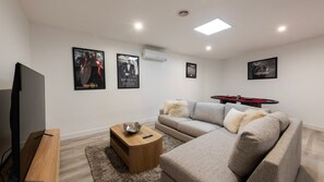 Een moderne woonkamer met een hoekbank, een flatscreen-tv en een pooltafel.