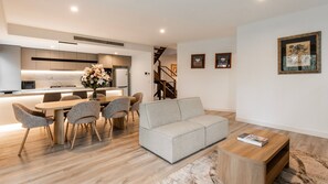 Uma sala de estar moderna com um sofá cinzento, mesa de centro de madeira e área de jantar com cadeiras e uma mesa.