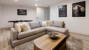 Uma sala de estar moderna com um sofá modular, uma mesa de centro de madeira e dois cartazes emoldurados na parede.