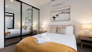 Quarto de hotel com cama grande, espelho, pintura e mesa de cabeceira com luminária.