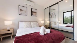 Ein modernes Hotelzimmer mit einem großen Bett, Nachttischlampen, einem Spiegel und Kunstwerken an den Wänden.