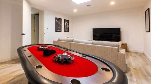 Ein Billardtisch mit roter Filzoberfläche, eine Couch, ein Fernseher und gerahmte Bilder an der Wand.