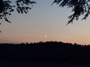 Ein sichelförmiger Mond am Himmel, mit Baum-Silhouetten am Horizont.