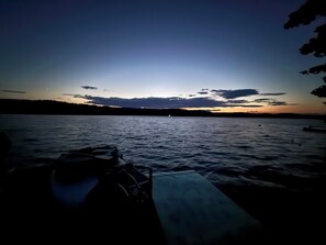 Ruhige Wasserfläche, auf der linken Seite ein Boot am Anleger und auf der rechten eine Bank.