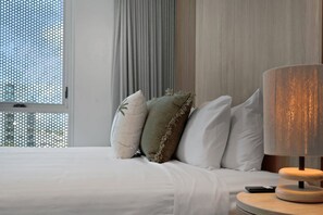 Ett hotellrum med en säng, kuddar, en lampa och ett fönster med gardiner.