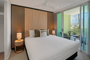 Ein Hotelzimmer mit einem großen Bett, zwei Nachttischlampen, einem Deckenventilator und einer Schiebeglastür zu einem Außenbereich mit Stuhl und Tisch.