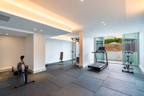 Ett modernt gym med träningsutrustning, ett löpband och en glasvägg som ger utsikt över en trädgård.