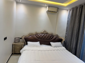 A bedroom with a large bed, a nightstand, a framed picture, and a wall-mounted air conditioner. - Cozy 1-bedroom apartment with AC in charming Dakar Almadie, comes with gym,pool (Dakar)