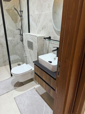 A modern bathroom with a glass-enclosed shower, a white toilet, and a wooden vanity with a mirror. - Cozy 1-bedroom apartment with AC in charming Dakar Almadie, comes with gym,pool (Dakar)