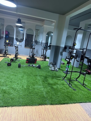 Un gimnasio con equipamiento de ejercicio, suelo de césped artificial y espejos en las paredes.