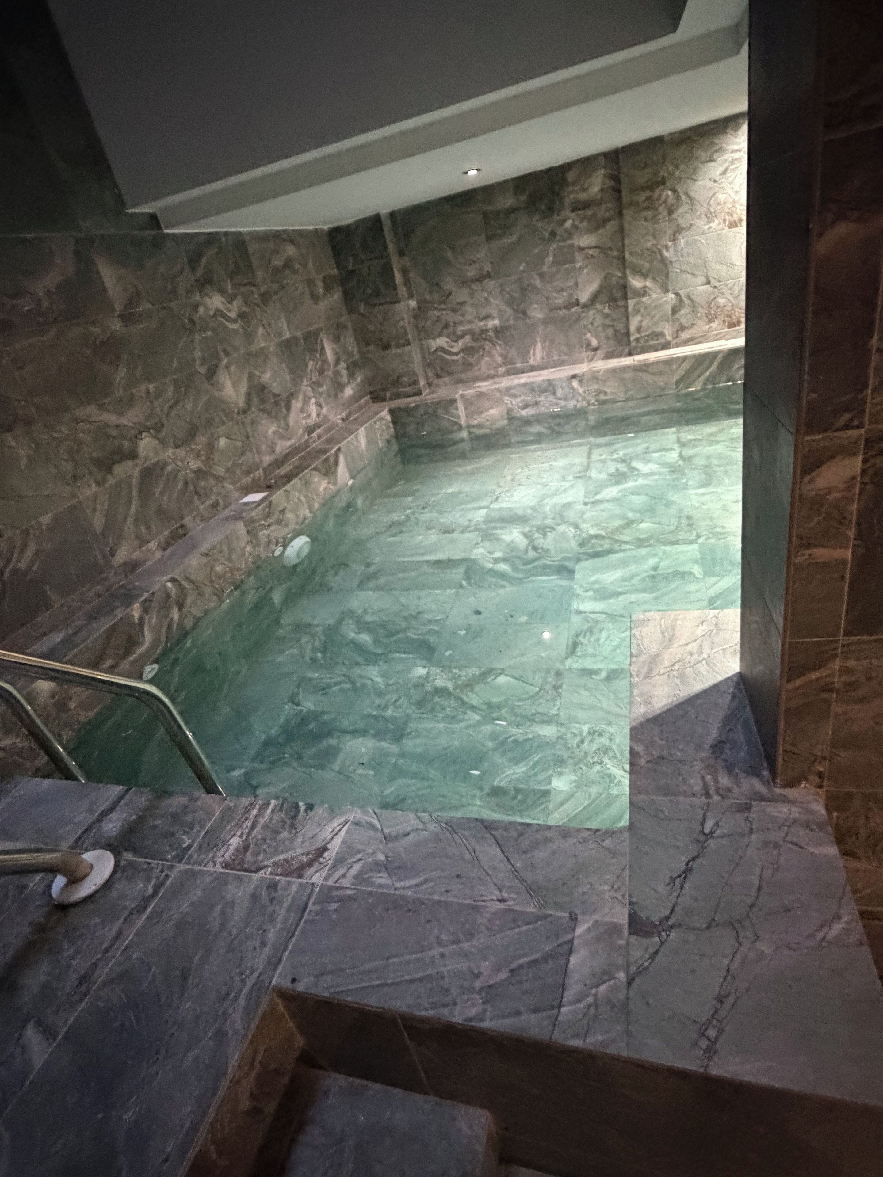 A stone-walled hot tub with clear water, a metal ladder, and a stone floor.