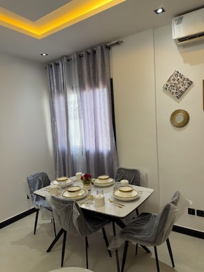 A dining area with a table set for four, covered chairs, and a modern ceiling design. - Cozy 1-bedroom apartment with AC in charming Dakar Almadie, comes with gym,pool (Dakar)