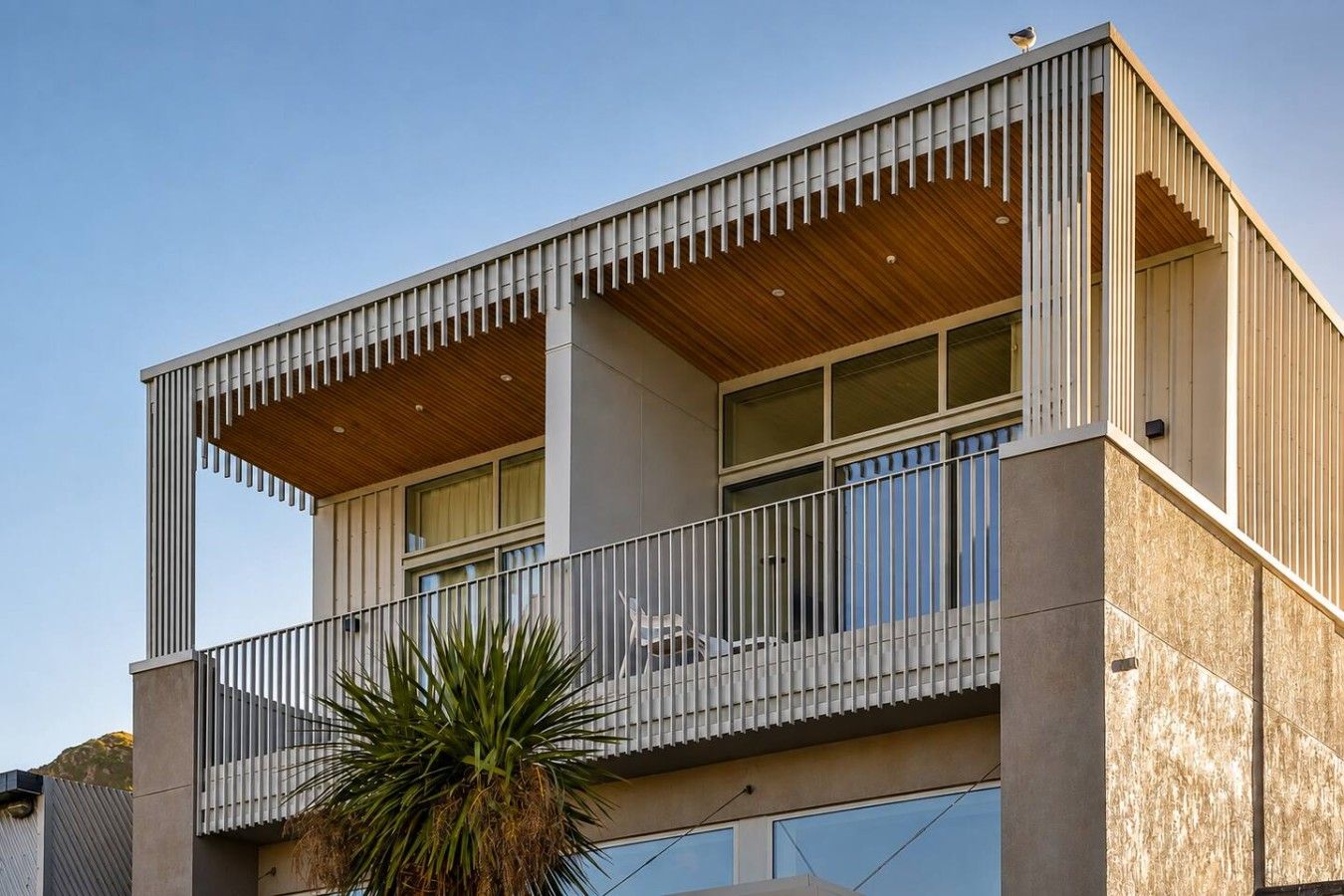 A modern two-story building with a balcony, large windows, and a wooden ceiling.