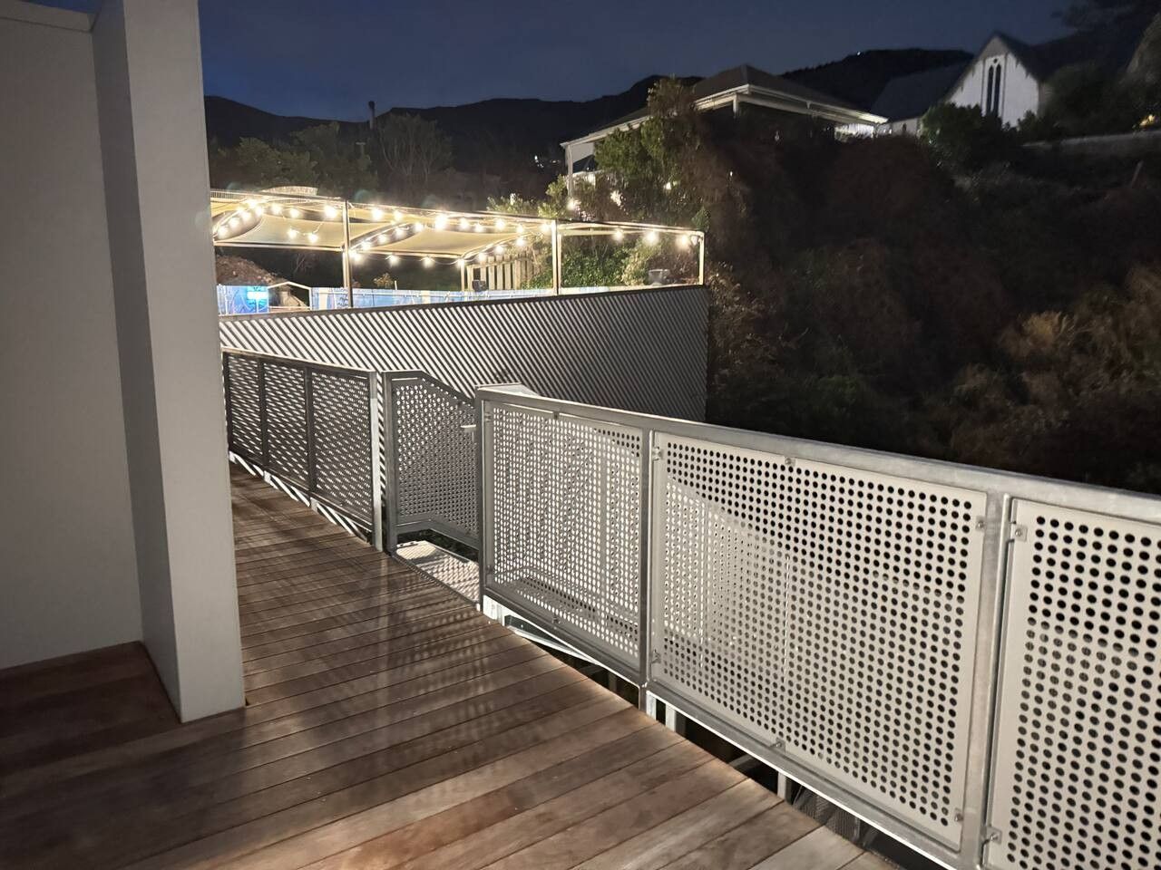A wooden deck with metal railings and a view of a lit-up area in the background.