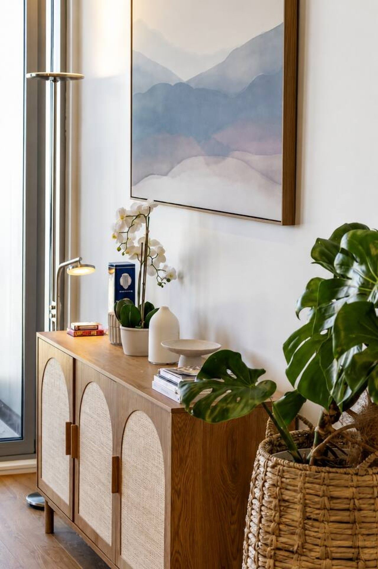 A wooden console with a white vase, a potted plant, and a lamp.