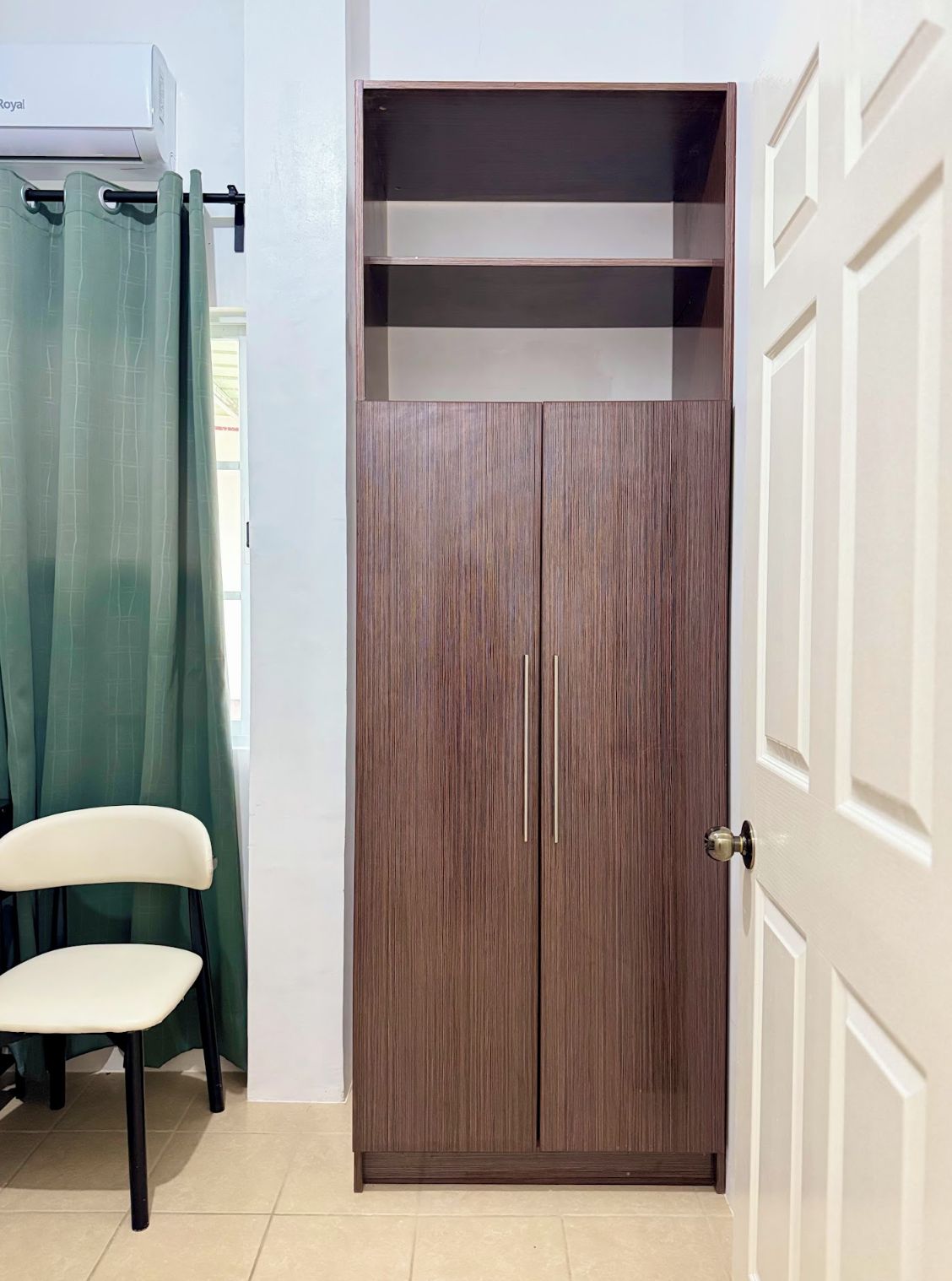 Ein Zimmer mit Schrank, Stuhl und Vorhang.