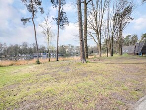 A grassy area with trees and a body of water in the background. - Beautiful bungalow with a canopy in nature (Stramproy)
