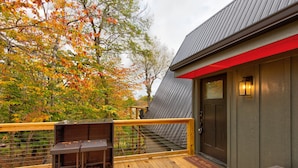 A wooden deck with a metal railing, a bench, and a door with a red accent. - LUXE | SKI-IN/OUT | Hot Tub | Fire Pit | A Frame (Beech Mountain)