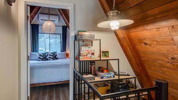 A cozy room with a bed, a shelf with books and games, and a hanging light fixture. - LUXE | SKI-IN/OUT | Hot Tub | Fire Pit | A Frame (Beech Mountain)