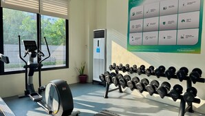 Une salle de sport équipée de matériel d’exercice, un tableau affichant les règles de la salle, et une fenêtre avec des stores.