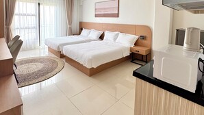 Une chambre d’hôtel avec un lit double, une table de salle à manger ronde, un coin cuisine et une grande fenêtre avec des rideaux.