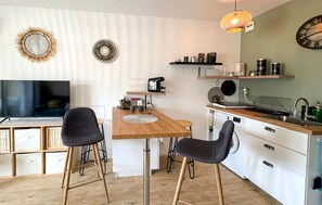 Eine moderne Küche mit einem Holztisch, zwei schwarzen Stühlen, einer Kaffeemaschine und einer Pendelleuchte.