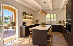 A modern kitchen with a central island, dark cabinetry, and a view to the outdoors. - Villa Avana avec Pisicne (Six-Fours-Les-Plages)
