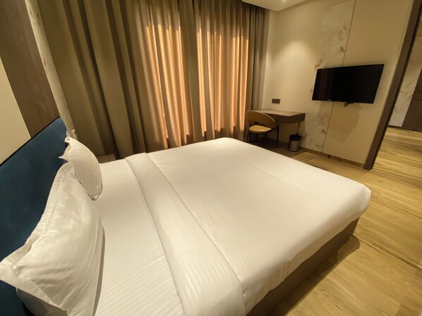 A hotel room with a bed, a desk, a chair, and a television on the wall.