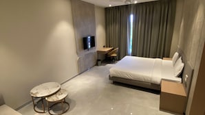 Ein modernes Hotelzimmer mit einem Bett, einer Sitzecke mit zwei runden Tischen, einem an der Wand befestigten Fernseher und einem Deckenventilator.