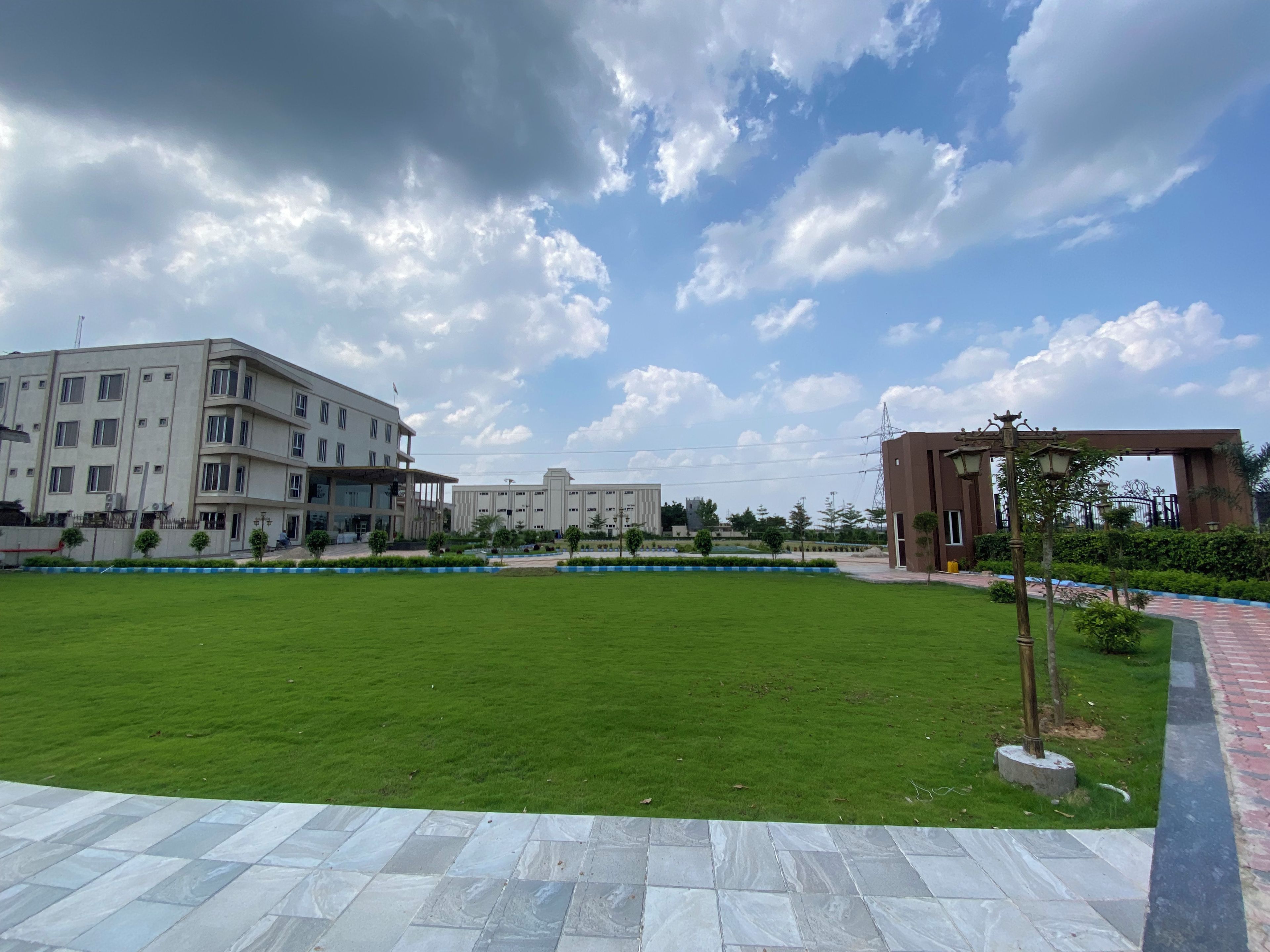 A spacious outdoor area with a well-maintained lawn, a paved walkway, and a modern building with multiple floors and large windows.
