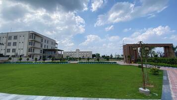 A spacious outdoor area with a well-maintained lawn, a paved walkway, and a modern building with multiple floors and large windows.