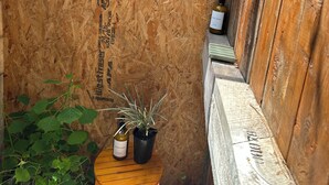 Un étroit couloir en bois, avec un banc en bois, une petite table sur laquelle se trouvent une bouteille et un pot de fleurs, et un mur orné d’un texte vertical.